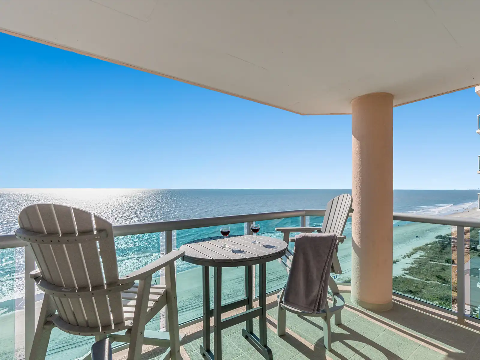 Oceanfront balcony with patio seating, a small table, and wine glasses