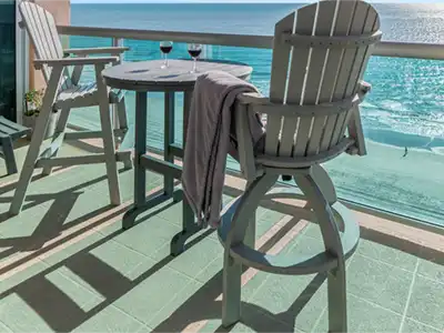 Two balcony chairs and a table with wine glasses, overlooking the ocean beach.