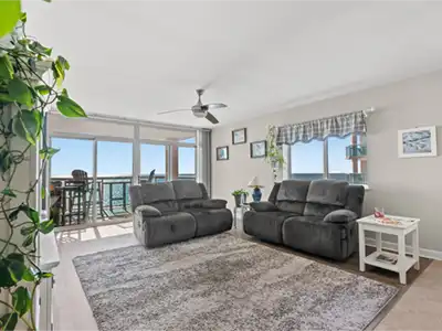 Bright living room with two gray sofas, a large rug, and sliding balcony doors.