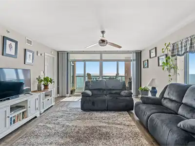 Bright living room with dark gray couches, a rug, and an ocean-view balcony.