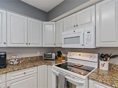 White kitchen cabinets, toaster oven, coffee maker, an electric stove, and a microwave.