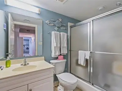 Blue bathroom with a white vanity, ocean decor, and frosted glass shower doors.