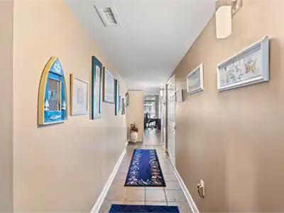 Hallway with tan walls, framed art, and a long blue patterned rug.