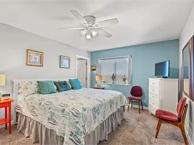 Bright coastal-style bedroom with TV, ceiling fan, and cozy king bed