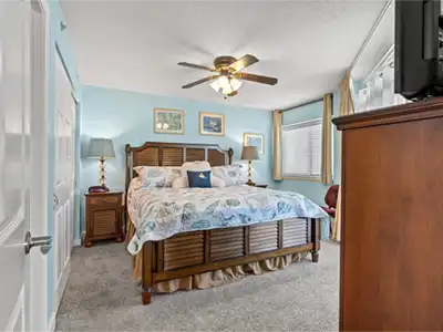 Cozy coastal-style king bedroom with TV, ceiling fan, and natural light